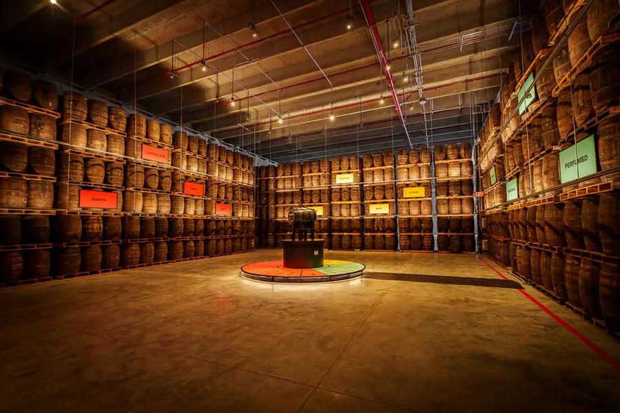 Almacén de añejamiento de BACARDÍ en Puerto Rico: barricas de ron en estanterías altas con carteles de aromas de colores y una plataforma redonda con barrica