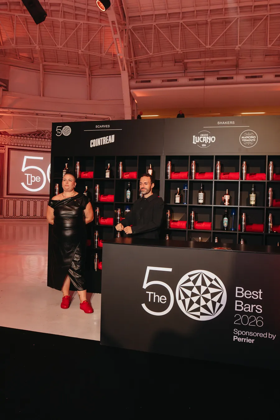 Cointreau en The 50 Best Bars 2026: pared de estanterías con bufandas rojas y botellas en el estand de Milán